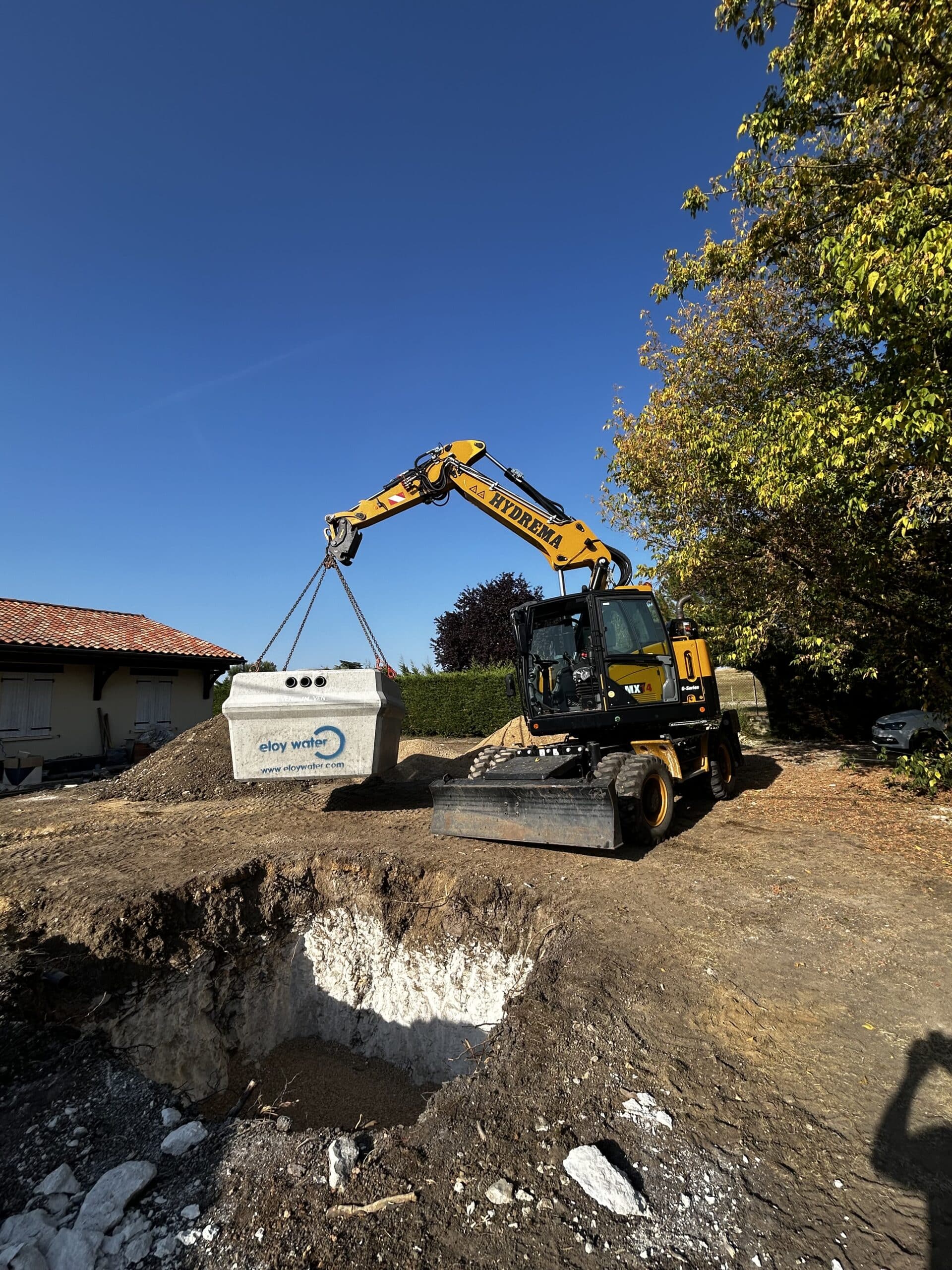 Excavation au Coucher du Soleil : Travaux Lourds et Lumière Dorée Godet d'excavatrice jaune déversant de la terre et des roches au coucher du soleil dans une carrière, créant une forte lueur dorée.