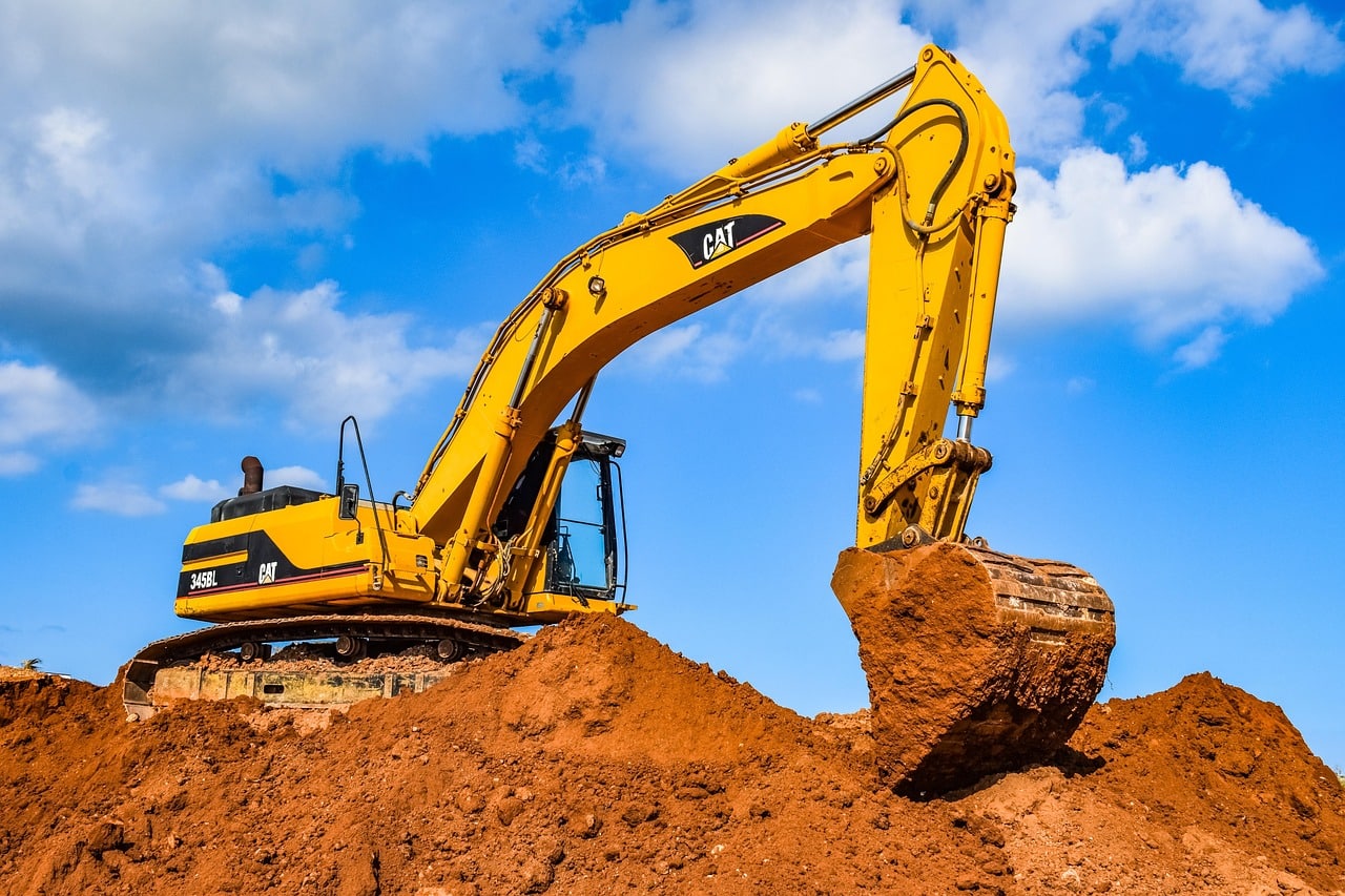 Excavation au Coucher du Soleil : Travaux Lourds et Lumière Dorée Godet d'excavatrice jaune déversant de la terre et des roches au coucher du soleil dans une carrière, créant une forte lueur dorée.
