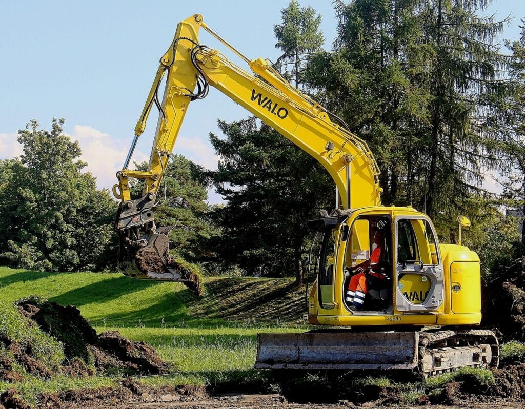 Pelle mécanique WALO jaune en action: Travaux de terrassement efficaces. Pelle mécanique WALO jaune sur chenilles creusant du gazon. L'opérateur déplace la terre lors de travaux de terrassement sous un ciel bleu.