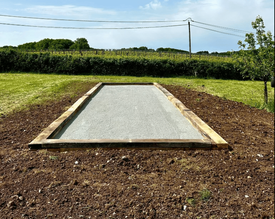 Terrain de pétanque en bois et gravier pour jardin privé Terrain de pétanque en bois et gravier gris dans un jardin avec vue sur un vignoble sous un ciel clair.
